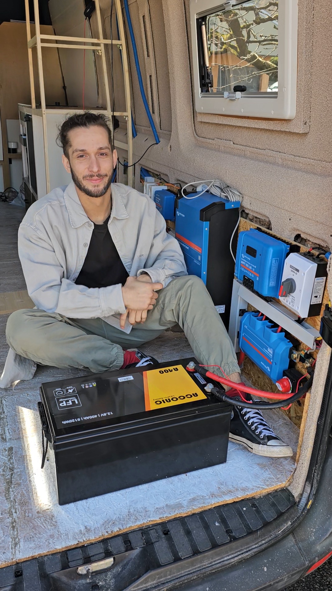 Gaël avec une batterie lithium devant l’installation électrique d’un van aménagé